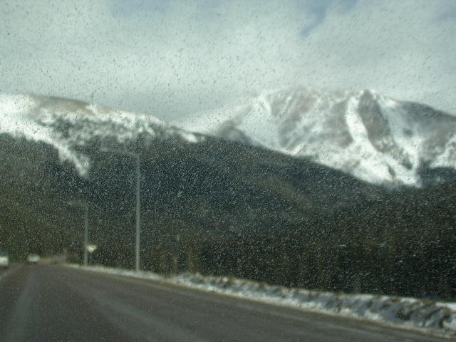 Road leading towards snow-capped mountains under a cloudy sky, seen through a speckled windshield