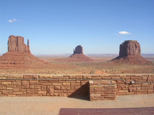 Monument Valley with mesas and buttes under a blue sky, viewed over a stone wall