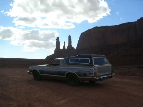 1975 Ford Ranchero - A 1975 Ford Ranchero, equipped with a camper shell, sits parked in a desert landscape with distinctive rock formations under a cloudy sky.