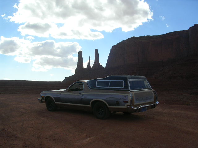 Two-tone brown and gray 1975 Ford Ranchero with camper shell parked in desert landscape