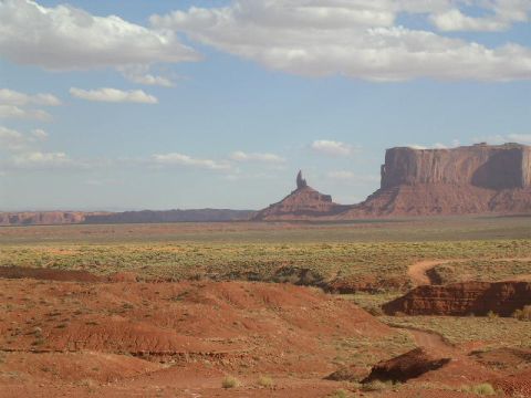 1975 Ford Ranchero - A vast desert landscape with iconic rock formations under a partly cloudy sky, a dirt road winding through the terrain.