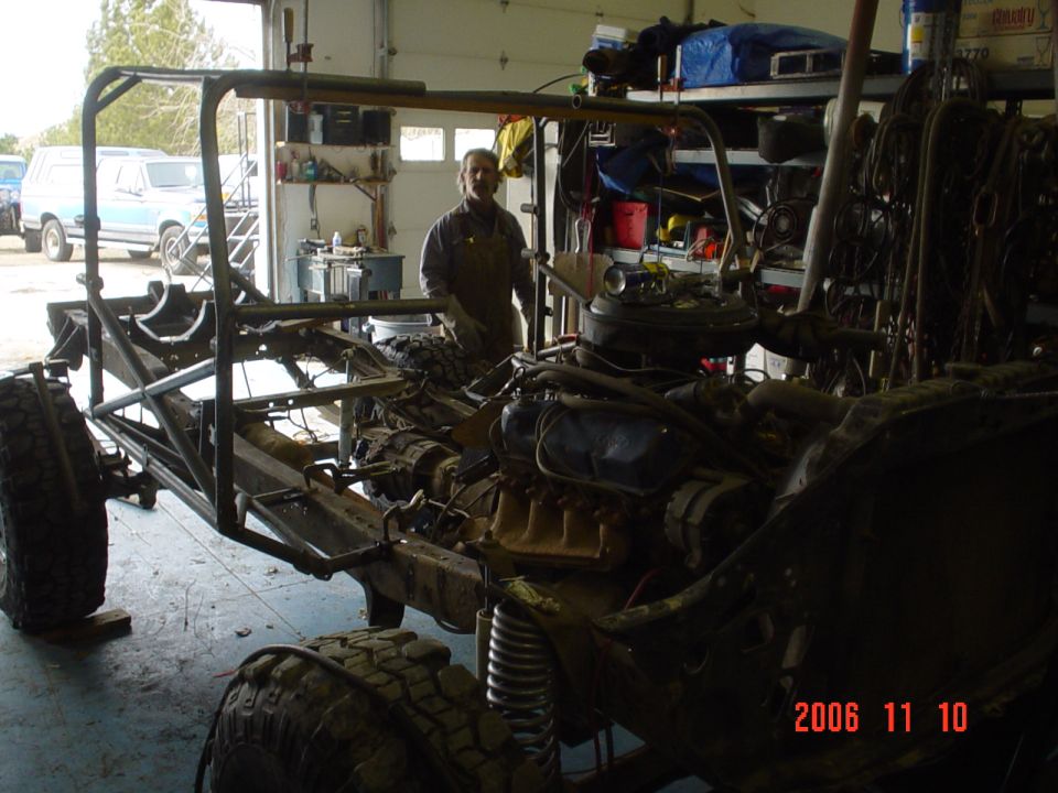 Vehicle chassis with engine and roll cage in a garage, viewed from the front