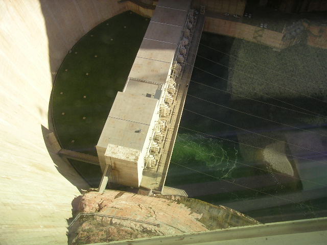 View from above of a large concrete dam structure with a reservoir of green water