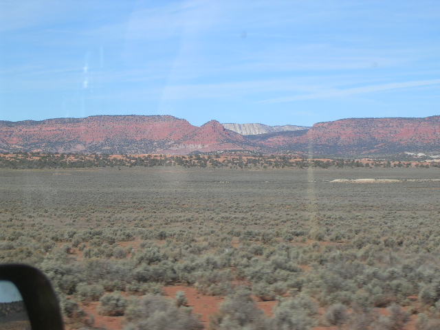 View of desert terrain and red rock mountains under a blue sky, seen from a vehicle