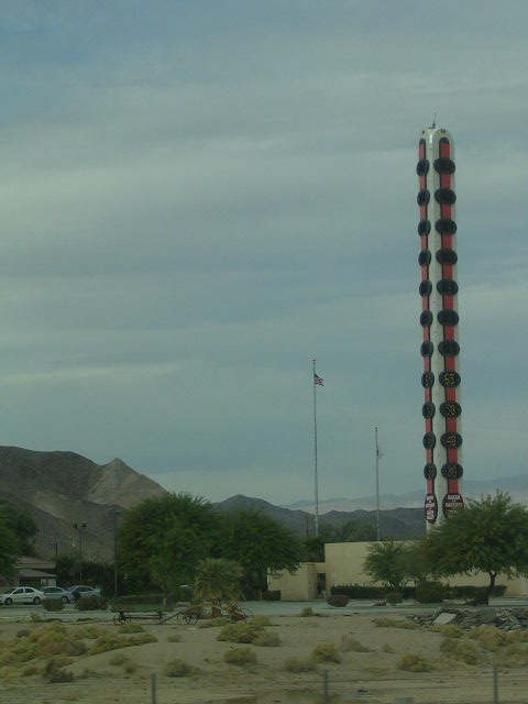 1975 Ford Ranchero - A giant thermometer roadside attraction stands tall against a cloudy sky, with flags and parked cars nearby.