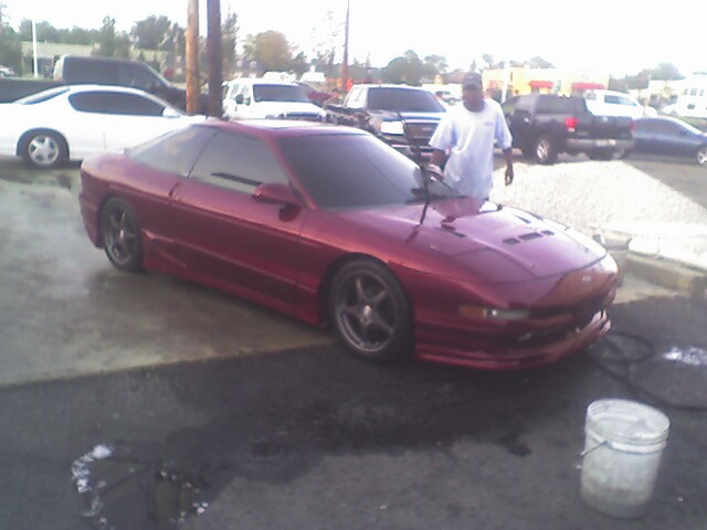 Red coupe with aftermarket wheels and body kit, seen from a 3/4 front angle