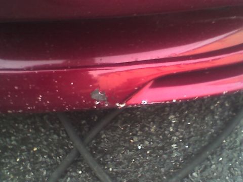 1994 Ford Probe - Scraped red car bumper shows chipped paint and damage.