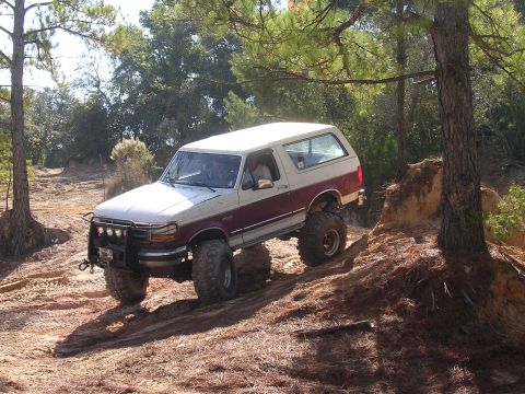 2006 Ford F-150 - A lifted Ford Bronco navigates an off-road trail with steep inclines and loose dirt.