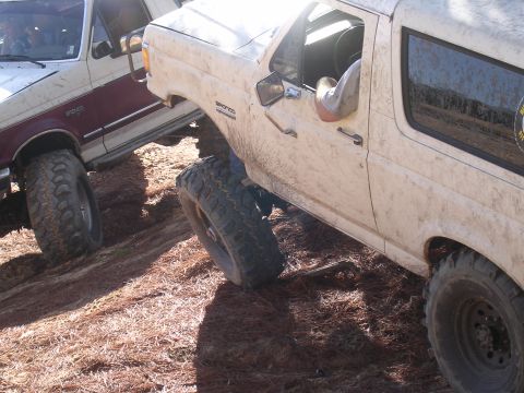2006 Ford F-150 - Two modified off-road vehicles are shown navigating a challenging, uneven terrain covered in pine needles.