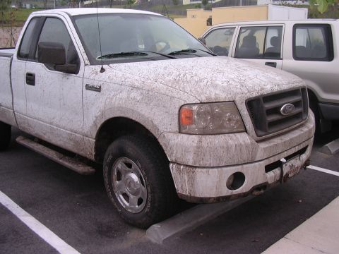 2006 Ford F-150 - A white Ford F-150 pickup truck is parked after being driven off-road, covered in mud.
