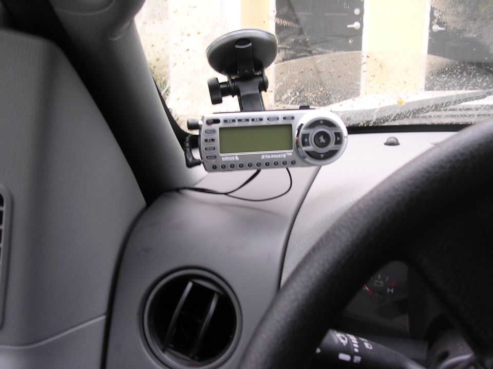 Dashboard interior with Sirius Starmate 8 receiver, suction cup mount, and part of steering wheel. Gray dashboard trim and air vent visible