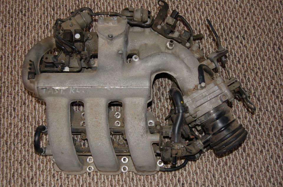 Engine intake manifold with "FAST KLS" written on it, on a carpeted surface