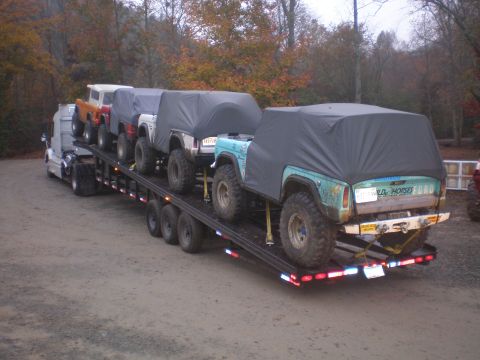 1969 Ford Bronco - A teal 1969 Ford Bronco, identified by its body style and visible text, is transported on a flatbed trailer alongside other vehicles.