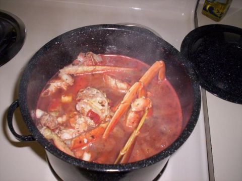 1989 Ford Bronco - A steaming black speckled enamel stockpot of tomato-based seafood stew with crab legs and shellfish simmering on a stovetop burner, lid set…