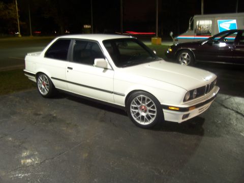 1992 Mercury Grand Marquis - A white BMW E30 coupe is seen from a 3/4 front angle, parked next to other vehicles at night.