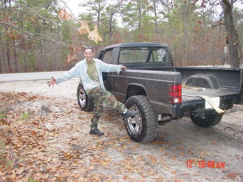 2004 Jeep Wrangler - A man poses with a dark Jeep Comanche pickup truck, its rear end prominently displayed. The vehicle's body style suggests an older model ye…