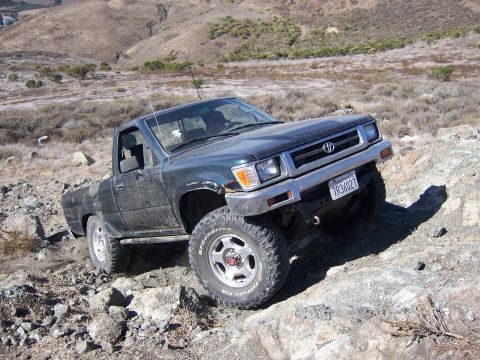 1995 Toyota Hilux - This Toyota pickup truck navigates a steep, rocky incline in a dry, hilly landscape.