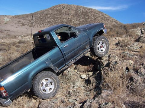 1995 Toyota Hilux - A teal pickup truck navigates a challenging rocky incline under a clear blue sky.