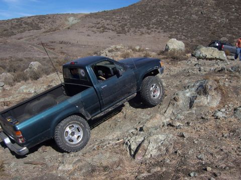 1995 Toyota Hilux - Pickup truck navigating a challenging rocky off-road course under a clear blue sky.