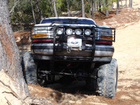 1989 Ford Bronco - Modified Ford F-Series truck with off-road modifications navigating a dirt trail.