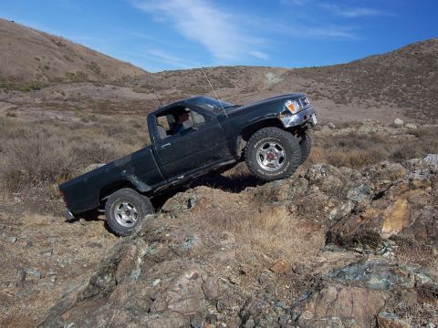 1995 Toyota Hilux - This truck is navigating a rocky trail with a driver inside. The vehicle appears to be a Toyota pickup from the early to mid-1990s.
