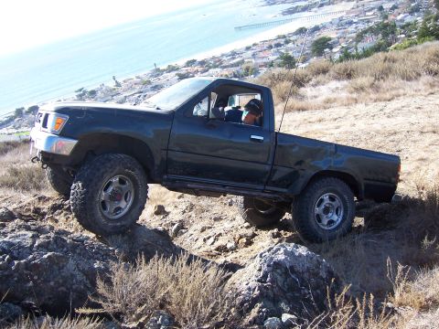 1995 Toyota Hilux - A dark green Toyota pickup truck is shown off-roading on a coastal hillside.