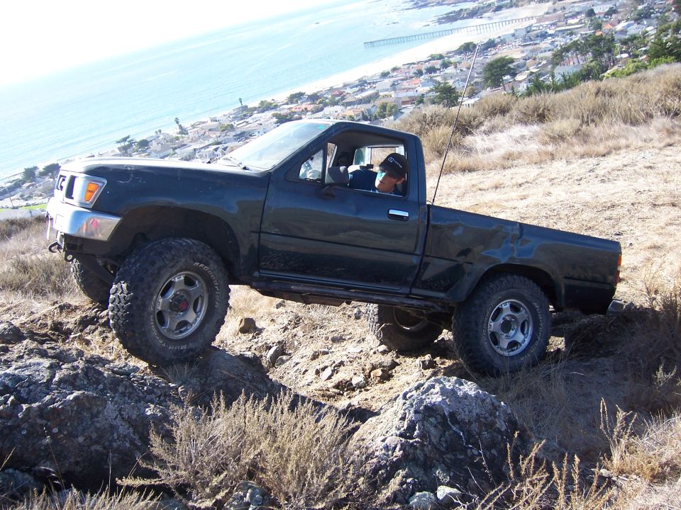Dark green Toyota pickup truck with off-road tires navigating rocky terrain