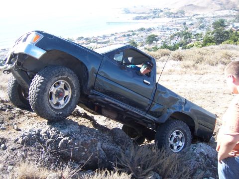 1995 Toyota Hilux - Pickup truck navigating rocky terrain with a coastal town in the background.