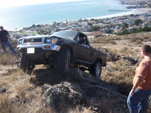1995 Toyota Hilux - Toyota Hilux navigates a challenging off-road course overlooking a coastal town.