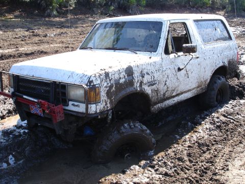1989 Ford Bronco - A white Ford Bronco is heavily caked in mud while stuck in a muddy terrain.