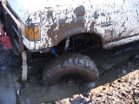 1989 Ford Bronco - A white 1989 Ford Bronco is deeply stuck in mud, with its front wheel submerged.
