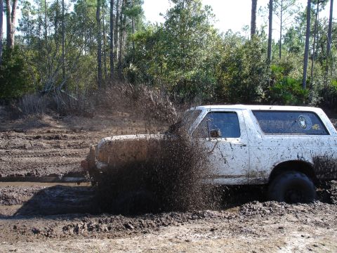 1989 Ford Bronco - Ford Bronco navigating a muddy trail with significant mud spray.