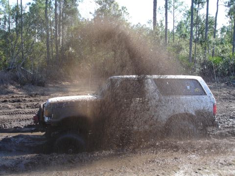 1989 Ford Bronco - A white 1989 Ford Bronco kicks up a large spray of mud while navigating a muddy trail.