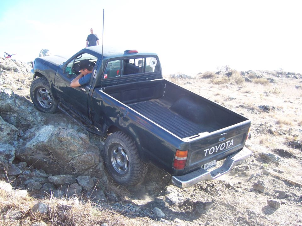 1995 Toyota Hilux driving over rocks on a dirt trail, driver visible inside