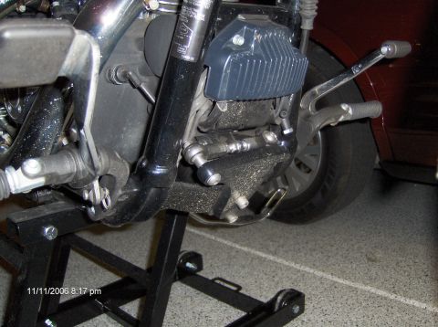 2004 Ford Crown Victoria - The motorcycle's engine and rear wheel are shown on a stand, with a car in the background.