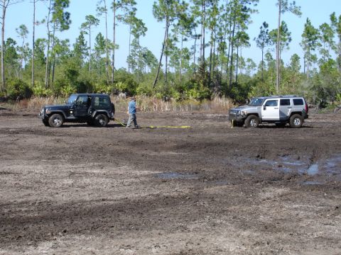 1989 Ford Bronco - Two off-road vehicles are stuck in the mud, with a person attempting to connect them with a tow strap.