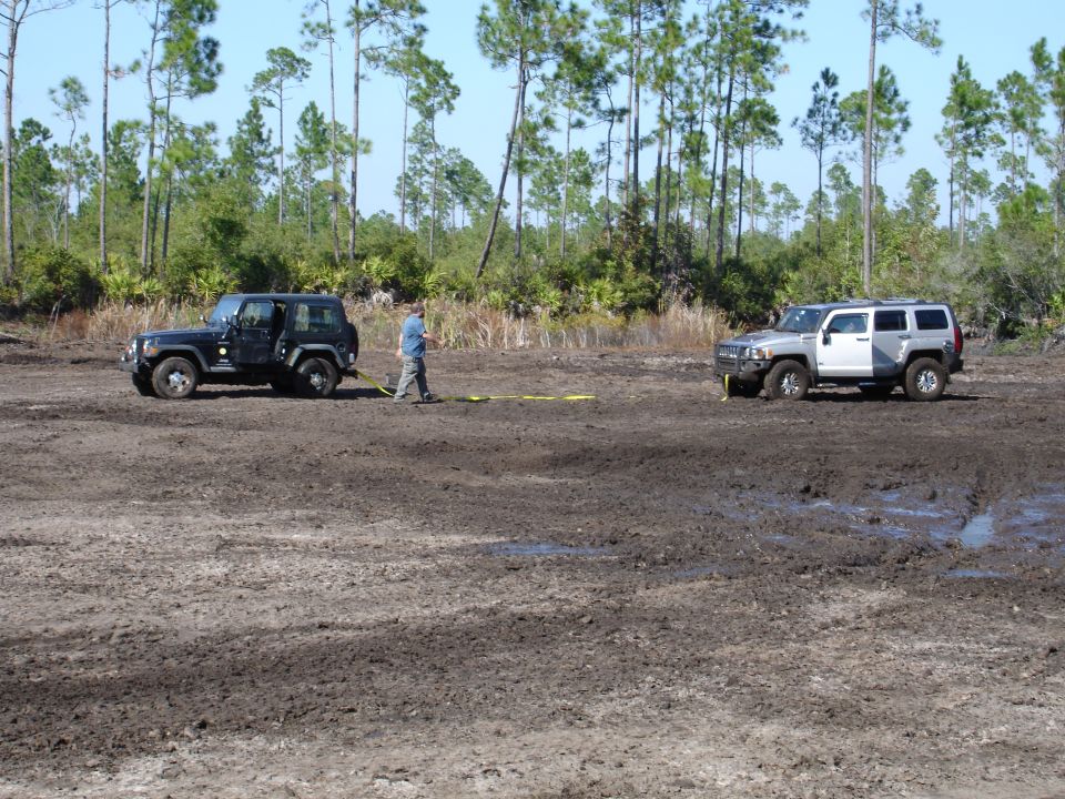 Black Jeep and silver Hummer in a muddy field with a person between them