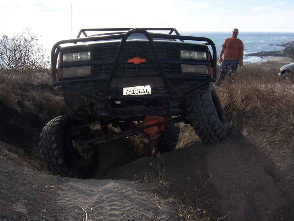 Lifted Chevrolet pickup with tube bumper flexing in a sand trench near the ocean