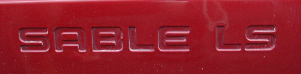 Embossed "SABLE LS" lettering on a dark red vehicle body panel