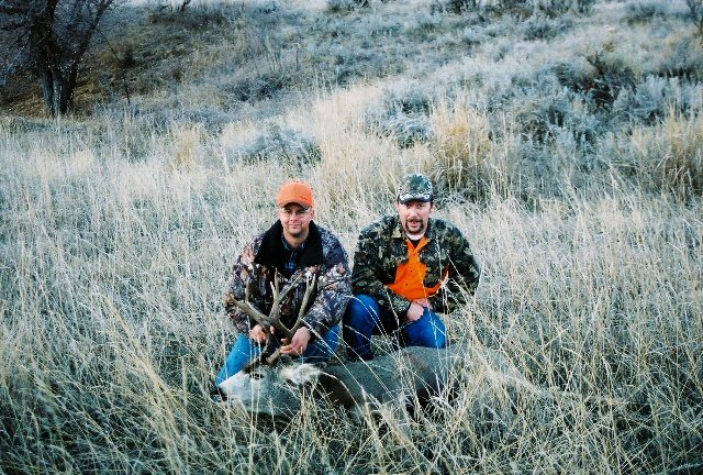 Two hunters pose with a deer in a field