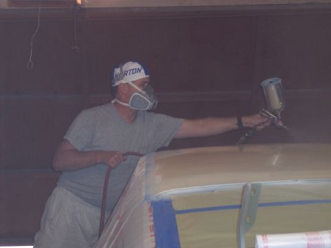 1971 Ford Mustang - A person in a respirator and hat sprays paint onto a car's roof, which is covered in masking tape.