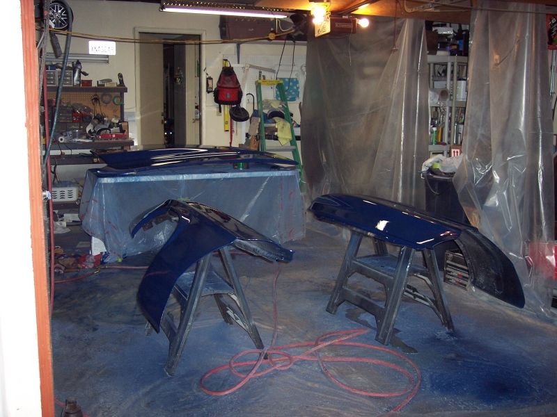 Dark blue car fenders and hood on sawhorses in a garage