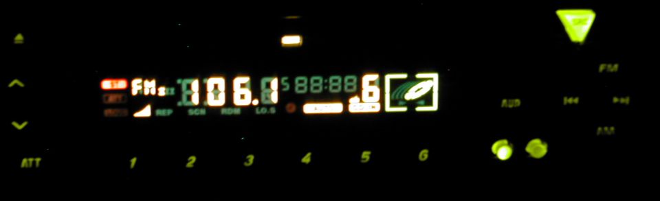 Illuminated car stereo display at night showing FM 106.1 with CD icon and preset buttons 1-6