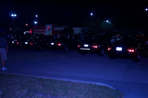 2006 Ford Mustang - A line of Ford Mustangs are parked in a lot at night, with one clearly displaying its model name on the rear.