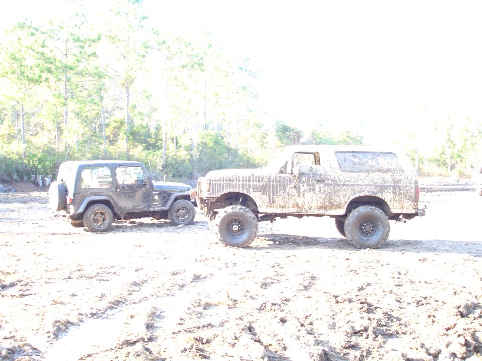 Mud-covered 1980s Ford Bronco and Jeep Wrangler parked on a dirt track