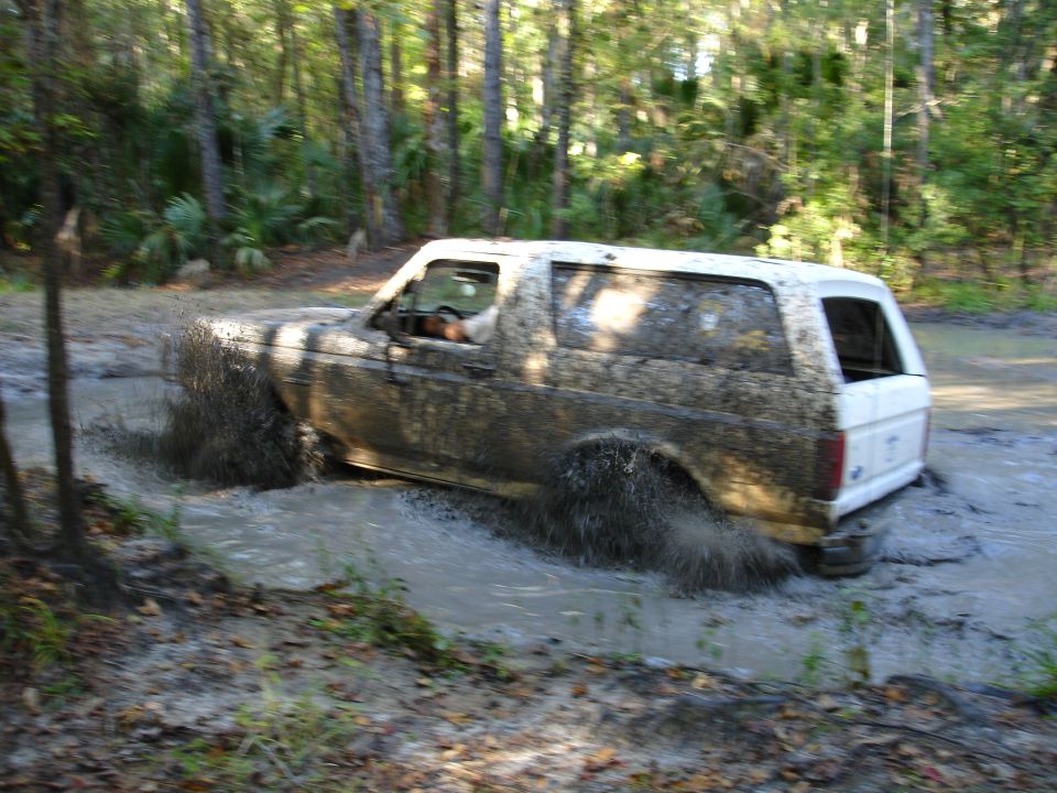 White 1989 Ford Bronco driving through mud, splashing water