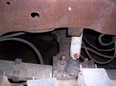 1995 Ford Bronco - Close-up of the undercarriage, showing leaf springs and a white shock absorber, with visible rust on the frame.