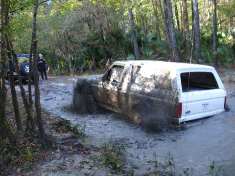 1989 Ford Bronco - White 1989 Ford Bronco is stuck in a muddy trail with another vehicle nearby.