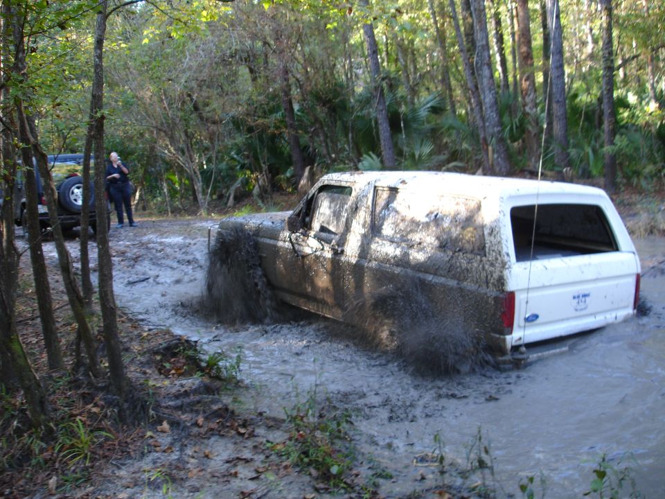 1989 Ford Bronco stuck deep in mud, another vehicle visible behind it