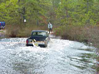 1988 Jeep Comanche - A Jeep pickup truck navigates through a watery terrain, kicking up spray.